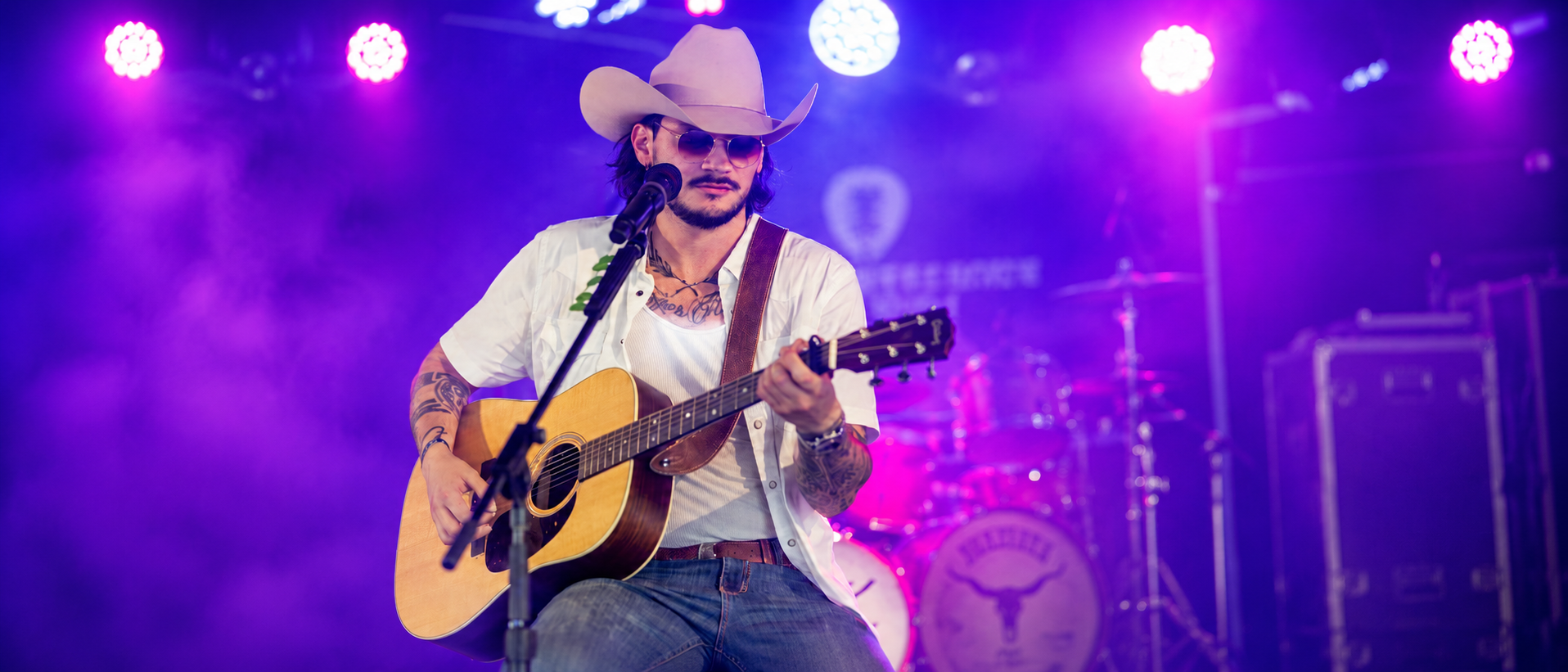 Anthony Segovia performing with an acoustic guitar under purple stage lights