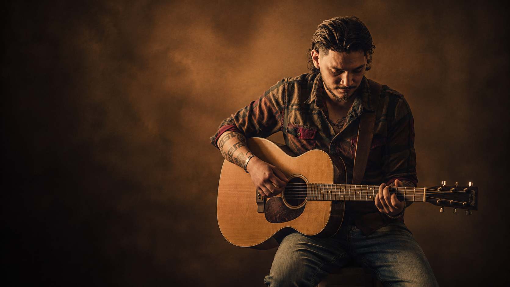 A guitarist holding an acoustic guitar in moody amber light